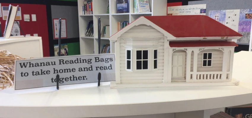 Shelf-topper — model of villa house with sign 'Whanau Reading Bags to take home and read together'
