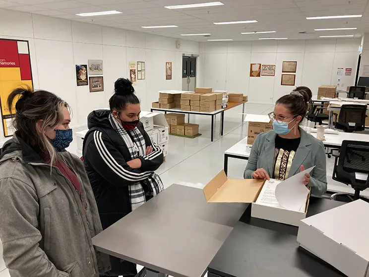 Two young Māori women being shown some documents held in an archive.