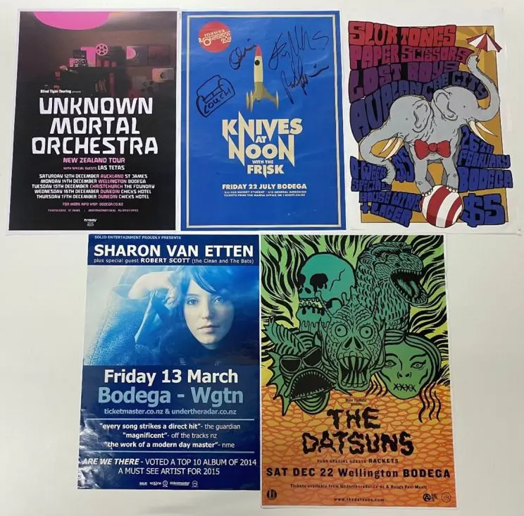 Five gig posters displayed on a table showing various colours and designs for bands like Unknown Mortal Orchestra, Knives at noon, and Sharon Van Etten. 