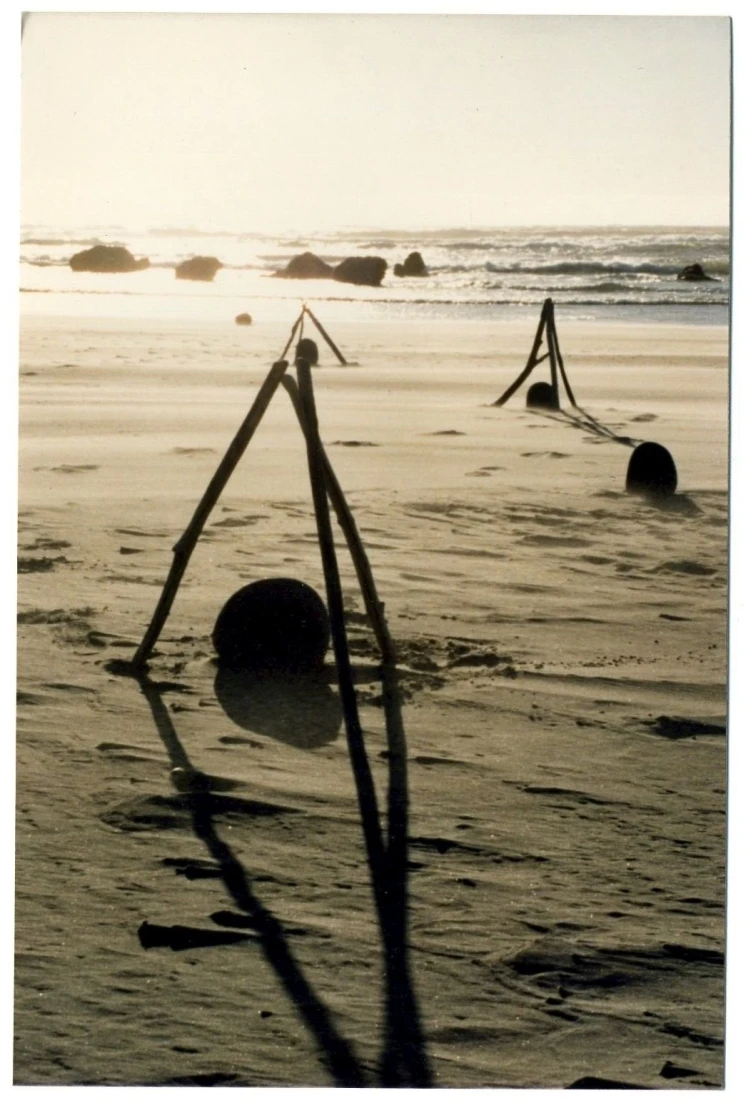 A scene on a beach showing three tripod sculptures made with driftwood.