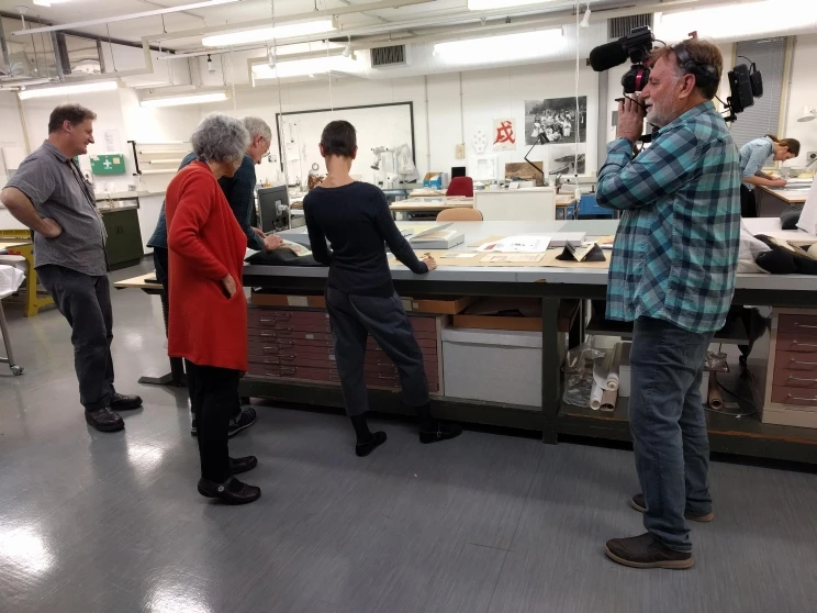 The cameraman with shoulder mounted camera films collection items displayed on a table while curatorial and conservation staff explain what they're doing.