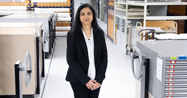 A woman wearing a black jacket and a white blouse in a room full of grey metal storage cabinets.