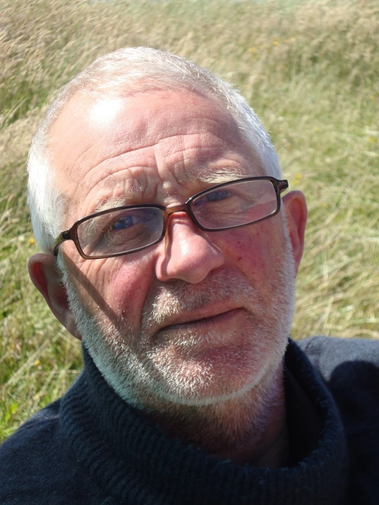 Portrait of a man with short white hair and beard and wearing glasses.