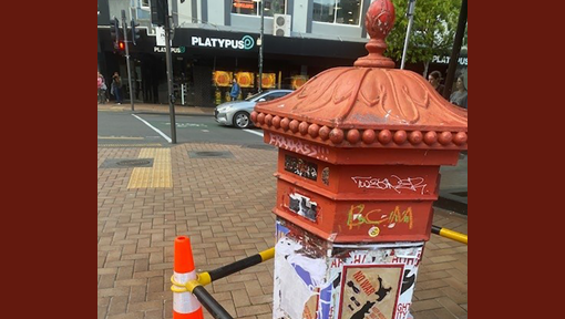 Red postbox with posters stuck on it. 