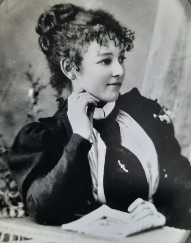 A black and white portrait of a woman seated at a table and looking off camera to her left.