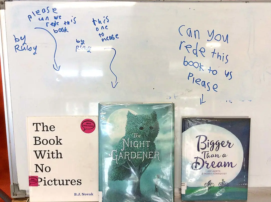 3 books in front of a whiteboard. The whiteboard has handwritten notes from tamariki requesting the books to be read to them. The books include, 'The Book With No Pictures' by B.J. Novak, 'The Night Gardener' by Terry Fan and Eric Fan, and 'Bigger Than a Dream' by Jef Aerts & Marit Törnqvist.