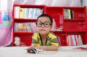 A young boy who is wearing glasses reading a book on the floor.