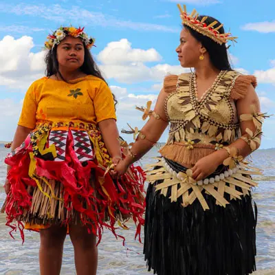 Two Pacific women holding hands standing in the sea.