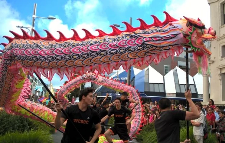 A Chinese dragon puppet is operated by four men who hold it aloft and animate the dragon using poles held in their hands.