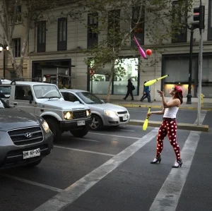 A woman with polka-dot pants and heels juggles in front of traffic halted at an intersection