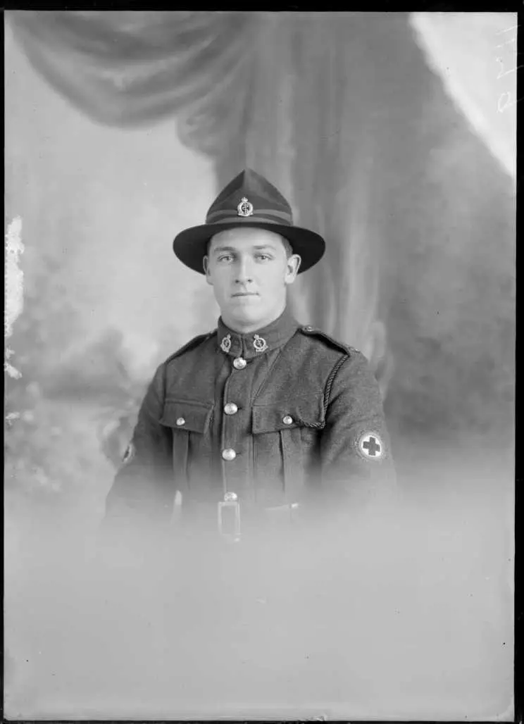 Studio upper torso portrait of an unidentified man dressed in a Medical Corps army uniform, showing the Red Cross badge on his left upper arm, with two badges on the lapels of his jacket, with a pin on his hat, possibly Christchurch district. Maclay, Adam Henry Pearson, 1873-1955, Negatives.