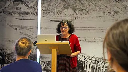 Kate De Goldi standing on a podium and speaking to participants at a Reading for Pleasure Hui in Auckland.