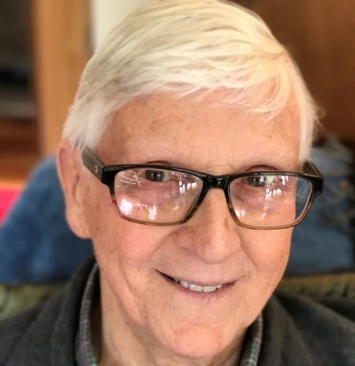 Portrait of a man wearing glasses and with white hair, smiling.