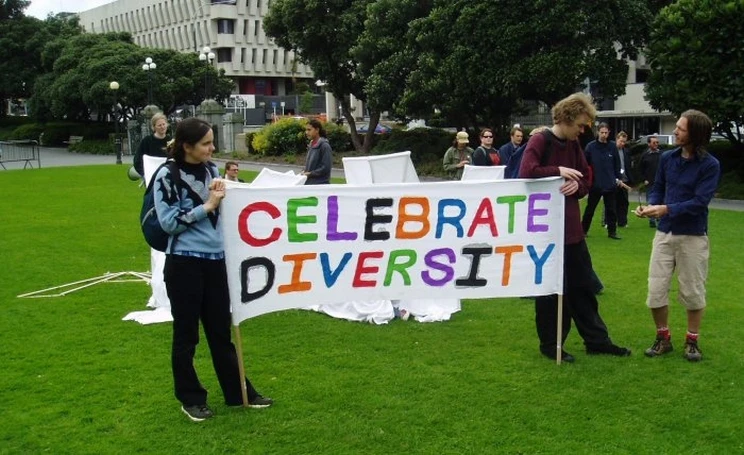 Two people standing on the green grass of Parliament grounds holding a large colourful sign that reads: Celebrate Diversity .