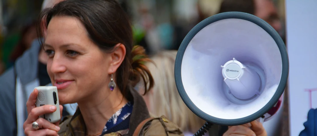 Woman with brown hair speaking into a megaphone microphone. 