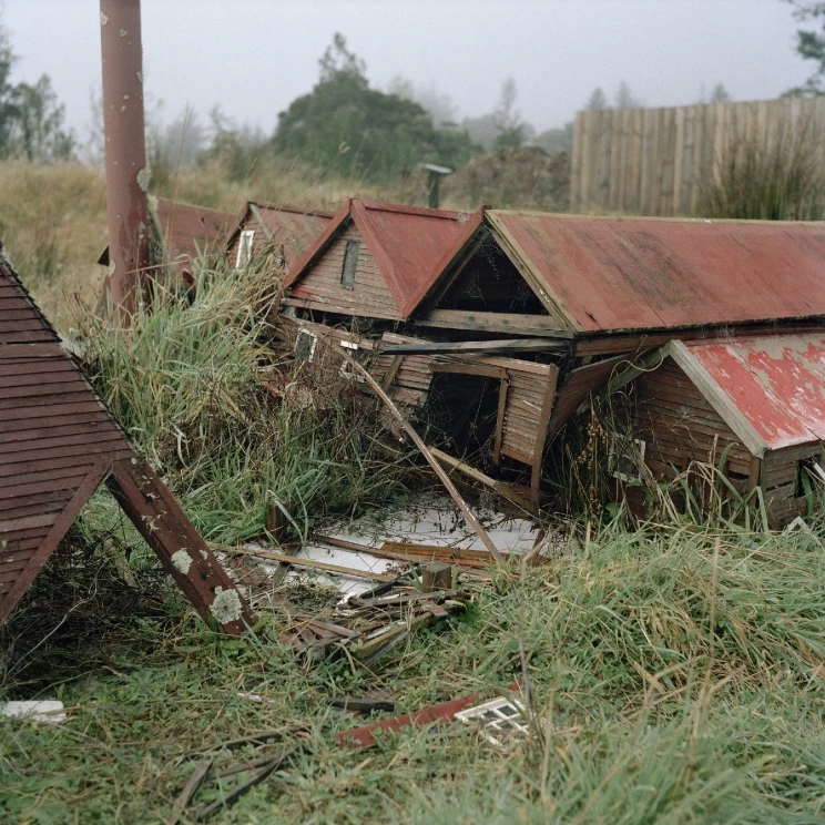 A miniature wooden building surrounded by tall grass is dilapidated and beginning to fall apart.