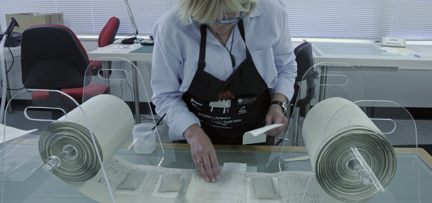 Conservator in lab joining pages of paper on 2 rolls together