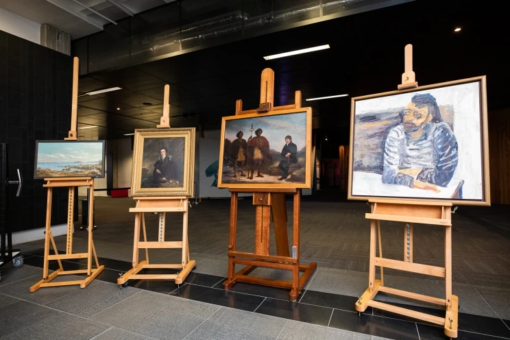 Four oil paintings each with a different frame and representing a different style are on display on easels.