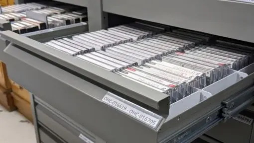 Cassette tapes are stored in grey archival drawers with labels. 