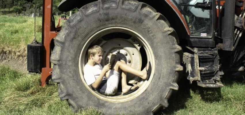 Boy in tractor wheel doing summer reading.