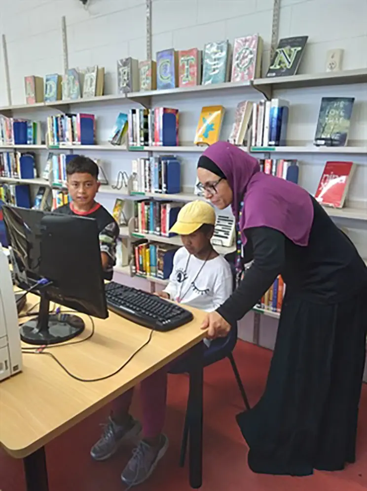 Muslim woman helping boys on a computer at a library. 