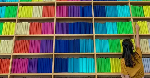 Woman with dark hair stands in front of shelves full of books organised in rainbow colours.