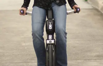 Shows the lower of Liane McGee  as she rides the YikeBike, a small foldable bicycle that is used in a regular sitting position. 