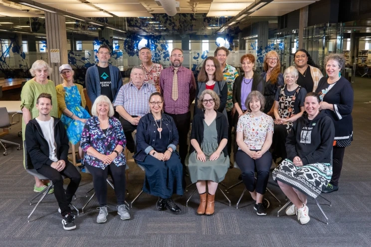 A group portrait taken in the reading room of the Alexander Turnbull Library of a diverse and friendly looking bunch of librarians.