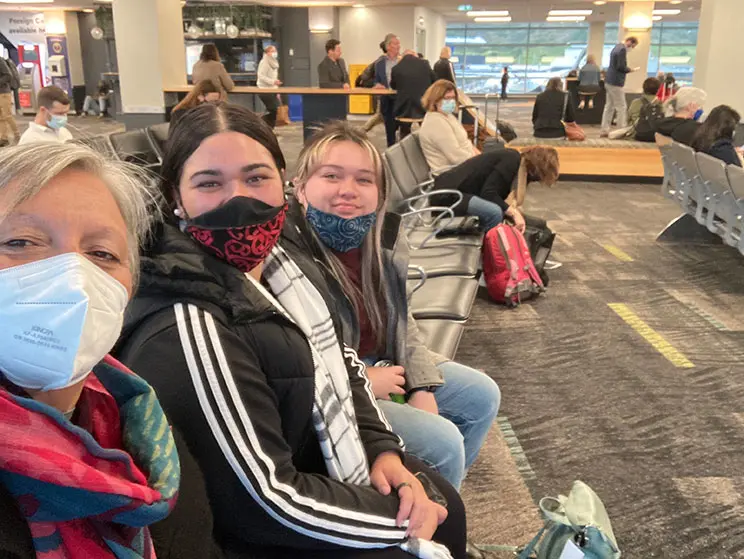 Selfie of three people wearing masks at an airport.