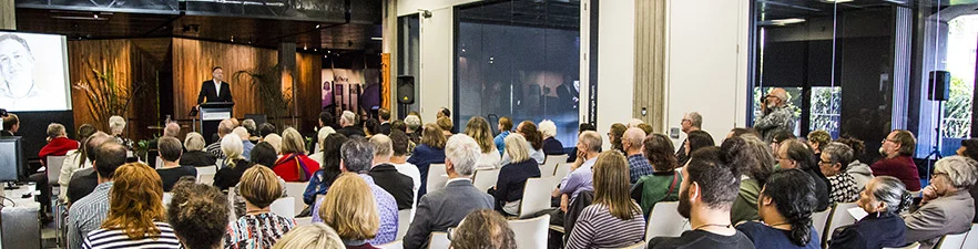 People seated at an event listening to a speaker. 