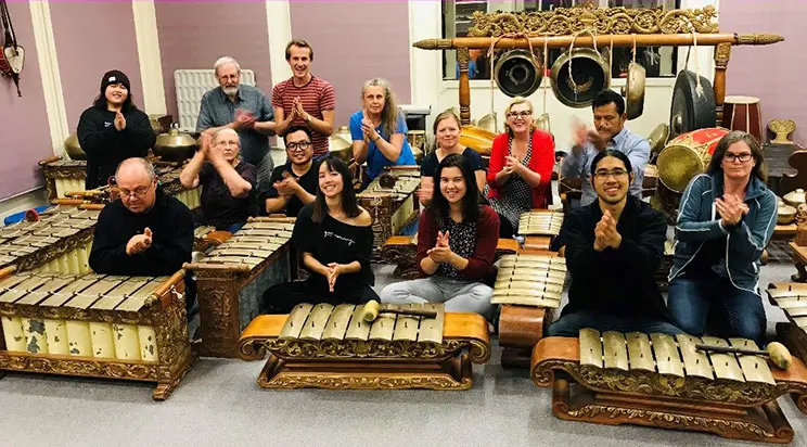 A group of people with xylophone style instruments in front of them. The people are holding their hands together. 
