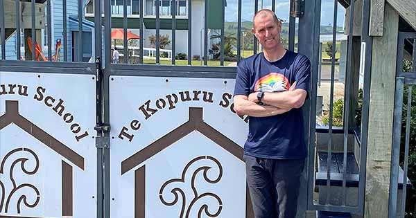 Te Awhi Rito Alan Dingley smiling and standing by the Te Kopuru School gate.