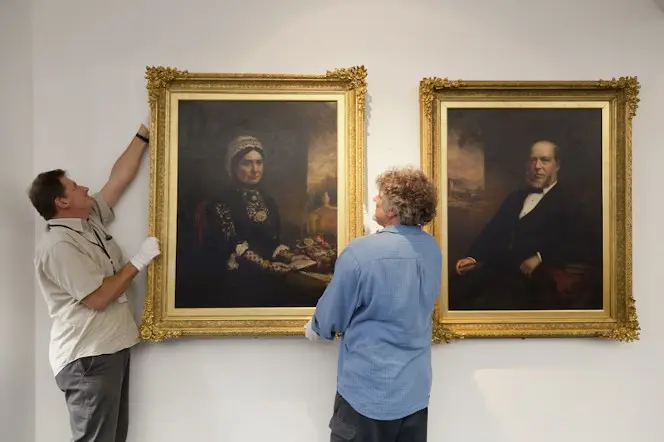 The two portraits being hung by staff.