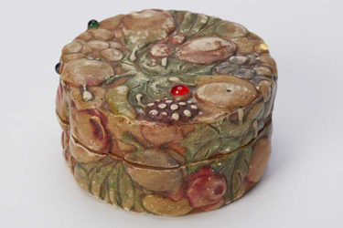 Small plaster container with Della Robbia-style fruits in a raised pattern on the lid. Inside are small flat mother-of-pearl incised shapes, of Chinese origin, some fish-shaped, some rectangular with patterns incised on them, part of a Chinese game.