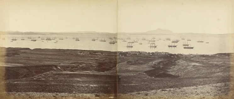 A faded yellow photo of a harbour with many boats of all sizes anchored in the water.