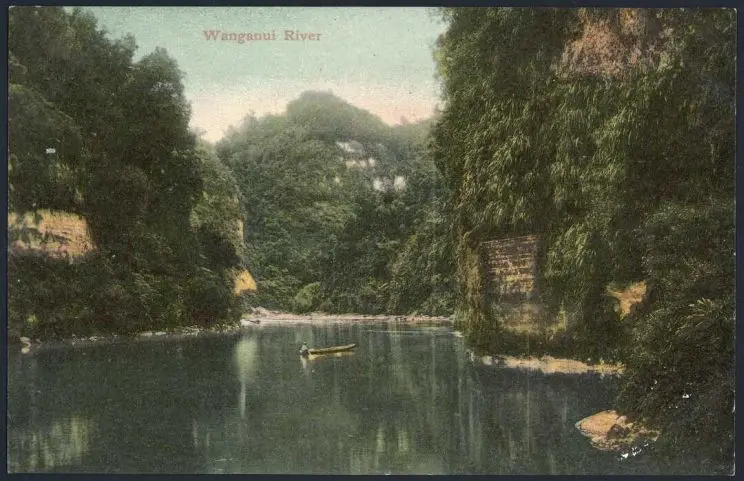 Shows a colourised photograph of a quiet scene in a gorge of the Wanganui River, with a figure seated in a boat in the centre of the image and tall, green-clad cliffs all around.