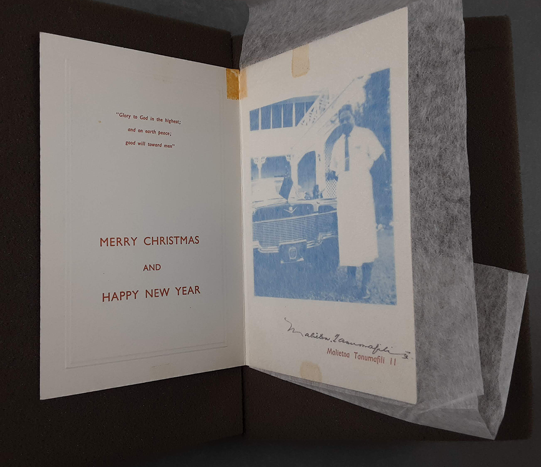 Inside of a Christmas card, on one side is a bible verse and words Merry Christmas and Happy New Year. On the other sideof a Samoan man standing by a car, the card is signed. 