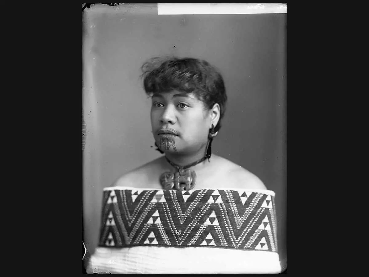 Black and white portrait photo of Pare Eru, who has a moko kauwae (a traditional Māori tattoo) above the lips and on the chin. Pare Eru has a hei tiki around the neck and is wearing a cloak, with a tāniko border, about the shoulders.