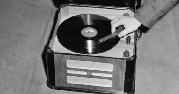 A gramophone with a record in it. A hand is lowering the tonearm.