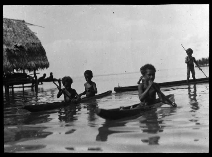 A group of children in small canoes are paddling around in calm water.