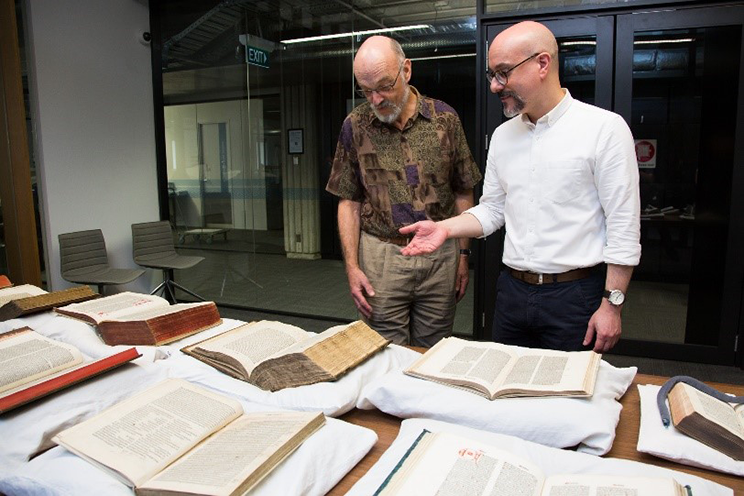 Two men looking at rare books on a table.