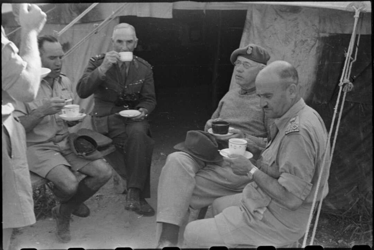 Group of military men sit in on chairs in an impromptu circle holding teacups and saucers.