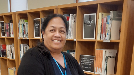 Māori woman standing in front of a bookshelf.