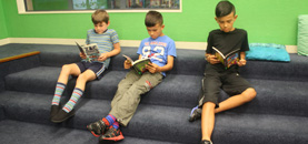 3 boys reading on carpeted steps inside the library.
