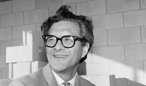 Portrait of a smiling Māori man wearing glasses and a suit.
