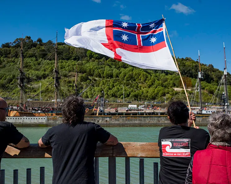 Protest looking over a harbour at a ship. They are waving the United Tribes flag.