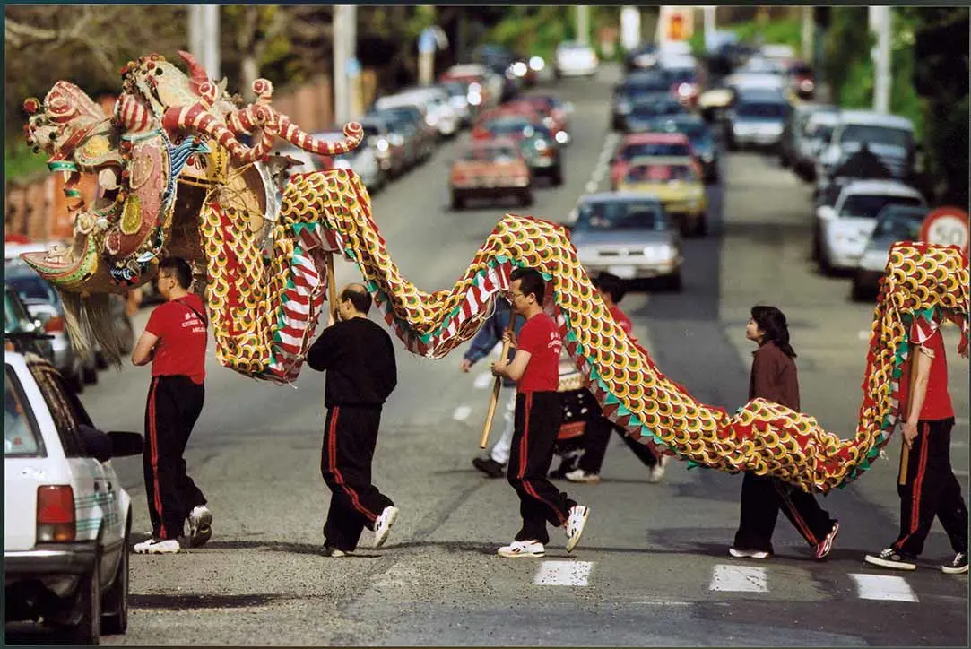 Colour photo of a Chinese giant dragon puppet being carried by 5 people across a street.