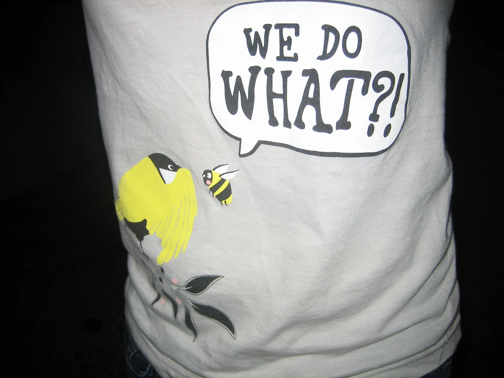 A white t-shirt with the image of a bee and a bird and the text 'We do What?!' in a speech bubble.