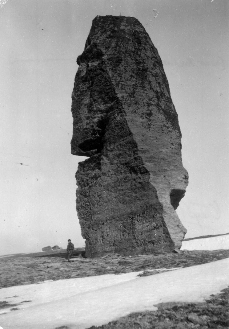 A man standing beside a huge rock is dwarfed by its size.