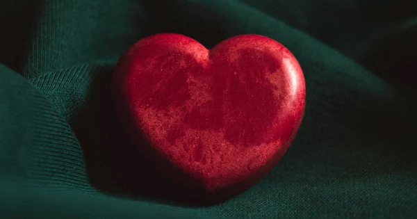 Photo of red heart sculpture sitting on folds of moss-green cloth. Image by Dhaya Eddine Bentaleb on Unsplash.